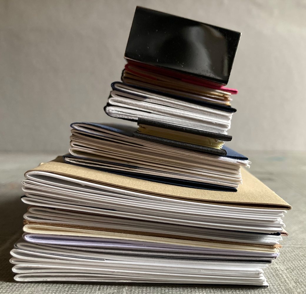 A pile of freshly bound sketchbooks with a chrome paperweight on top