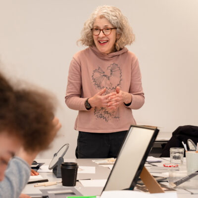 Lydia leading the self portrait workshop. In the foreground are mirrors, materials and a participant working