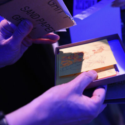 Lydia's hands showing the sketches in the box at the end of the event. The photograph shows the text on the underside of a piece of sandpaper