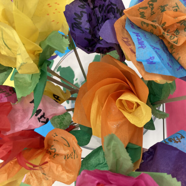 Tissue paper flowers with writing on petals and leaves, arranged in a glass vase
